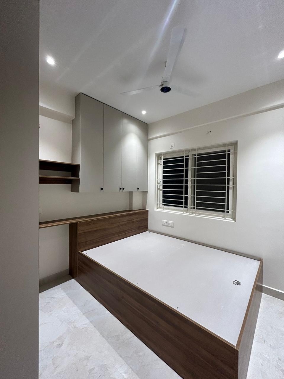 Finished compact bedroom with wooden platform bed overhead cabinets and window grill