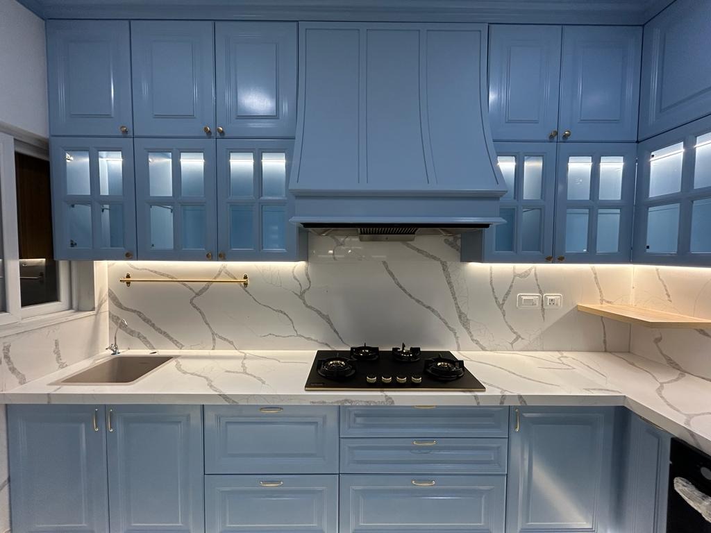 Close-up shot of blue kitchen counter, black stove, marble splashback and custom glass cabinet details