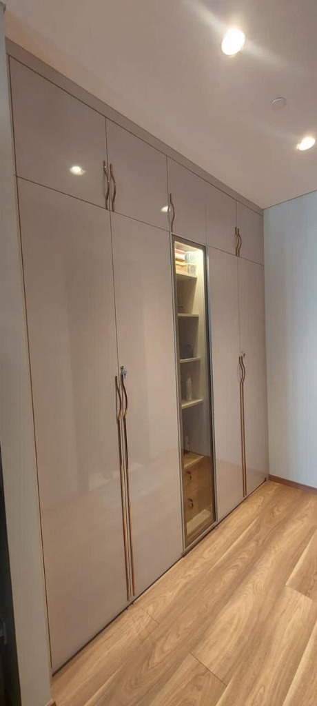 Modern gloss taupe bedroom wardrobe featuring gold designer handles and a glass partition lit display cabinet
